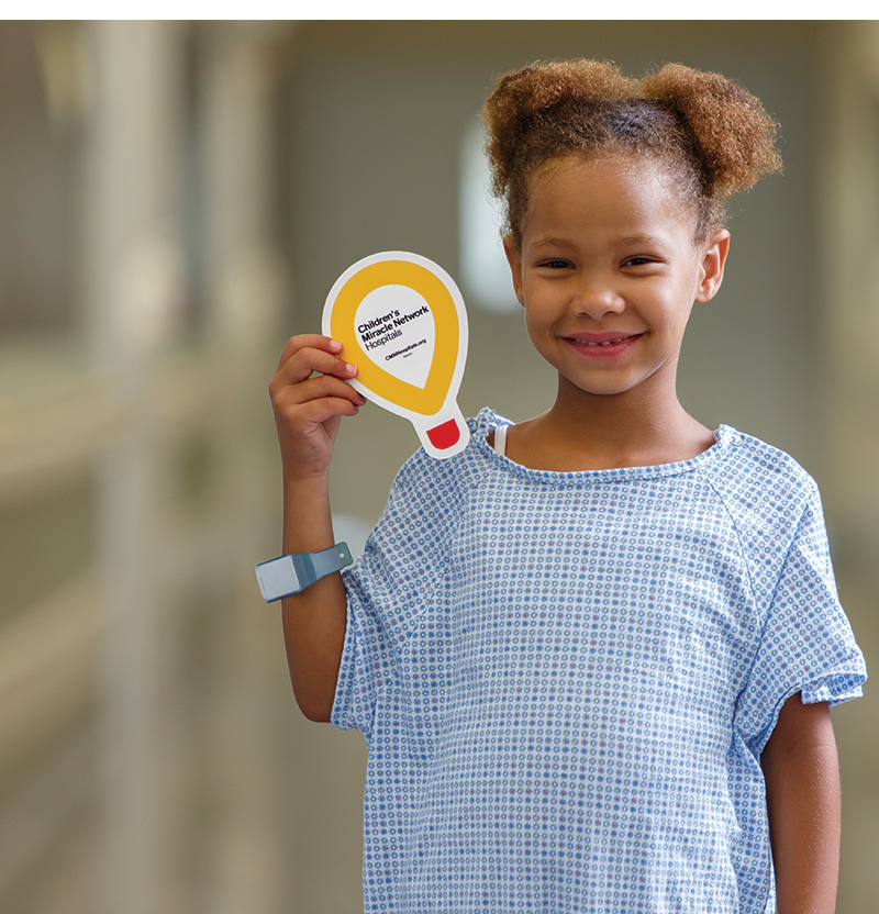 girl in hospital gown holding yellow paper balloon.