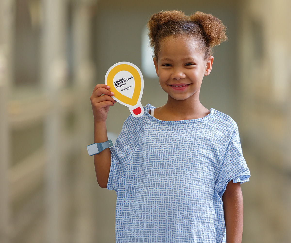 girl in hospital gown holding yellow paper balloon.