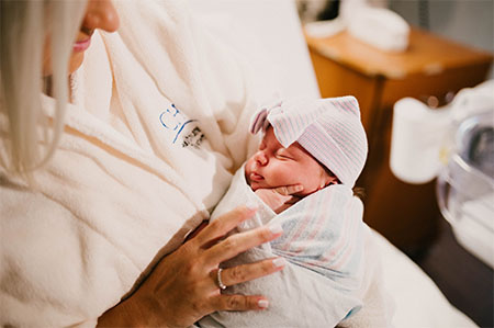 mother wearing bathrobe with swaddled newborn.